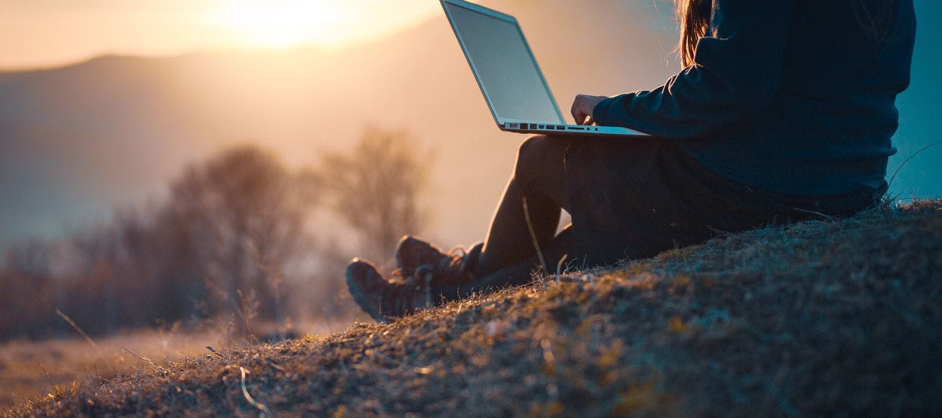 Bilde av dame som sitter ute i naturen og jobber på en laptop