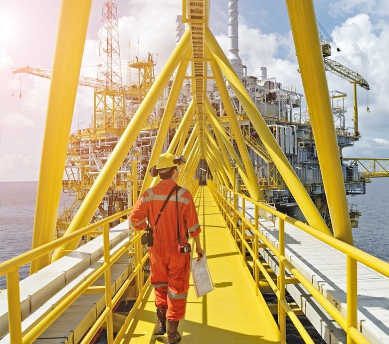 Bilde fra en oljeplattform der en mann går på en gul gangbro mellom to enheter
