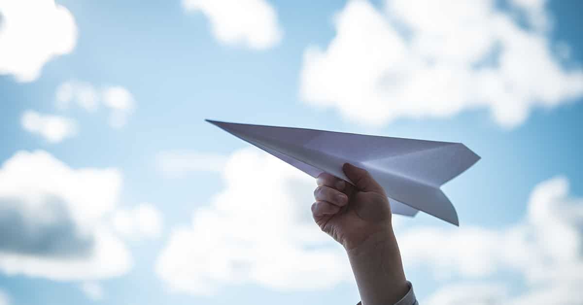 En hånd holder et papirfly og er klar til å sende det avgårde