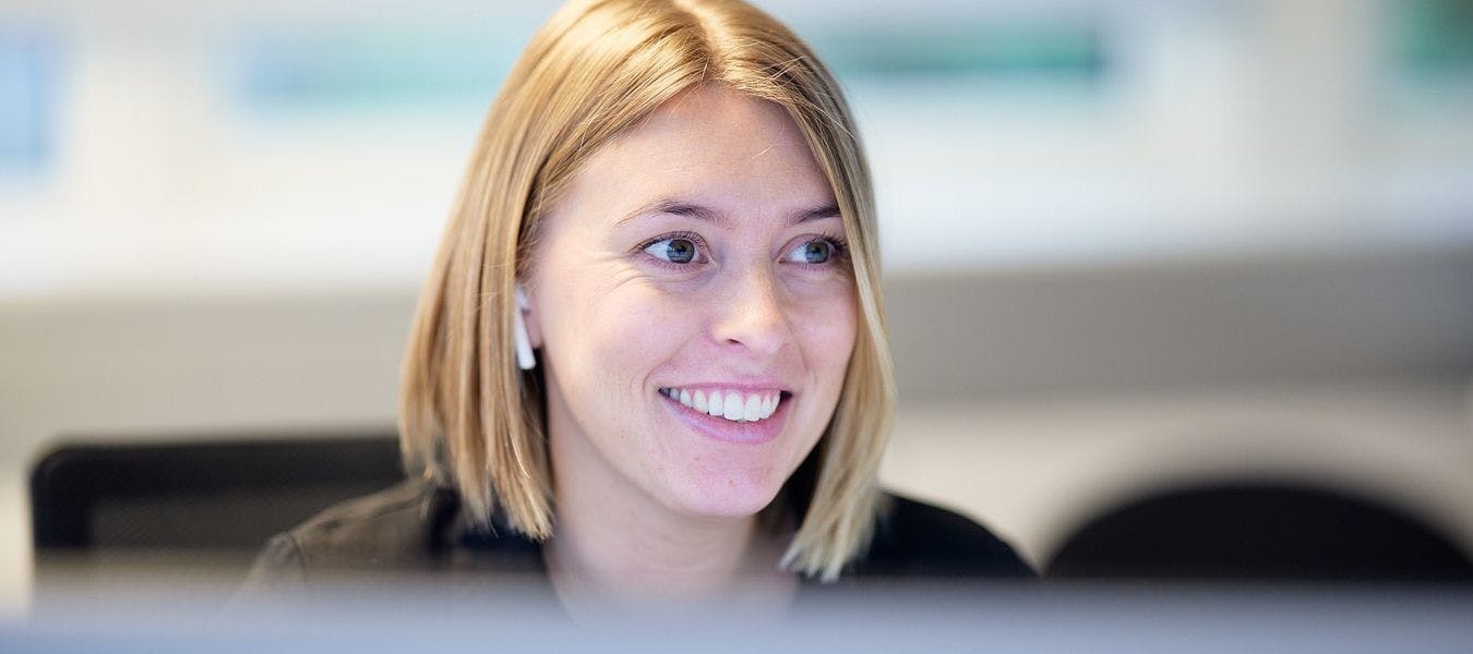 Nærbilde av en smilende damene med halvlangt blondt hår som jobber på kontor